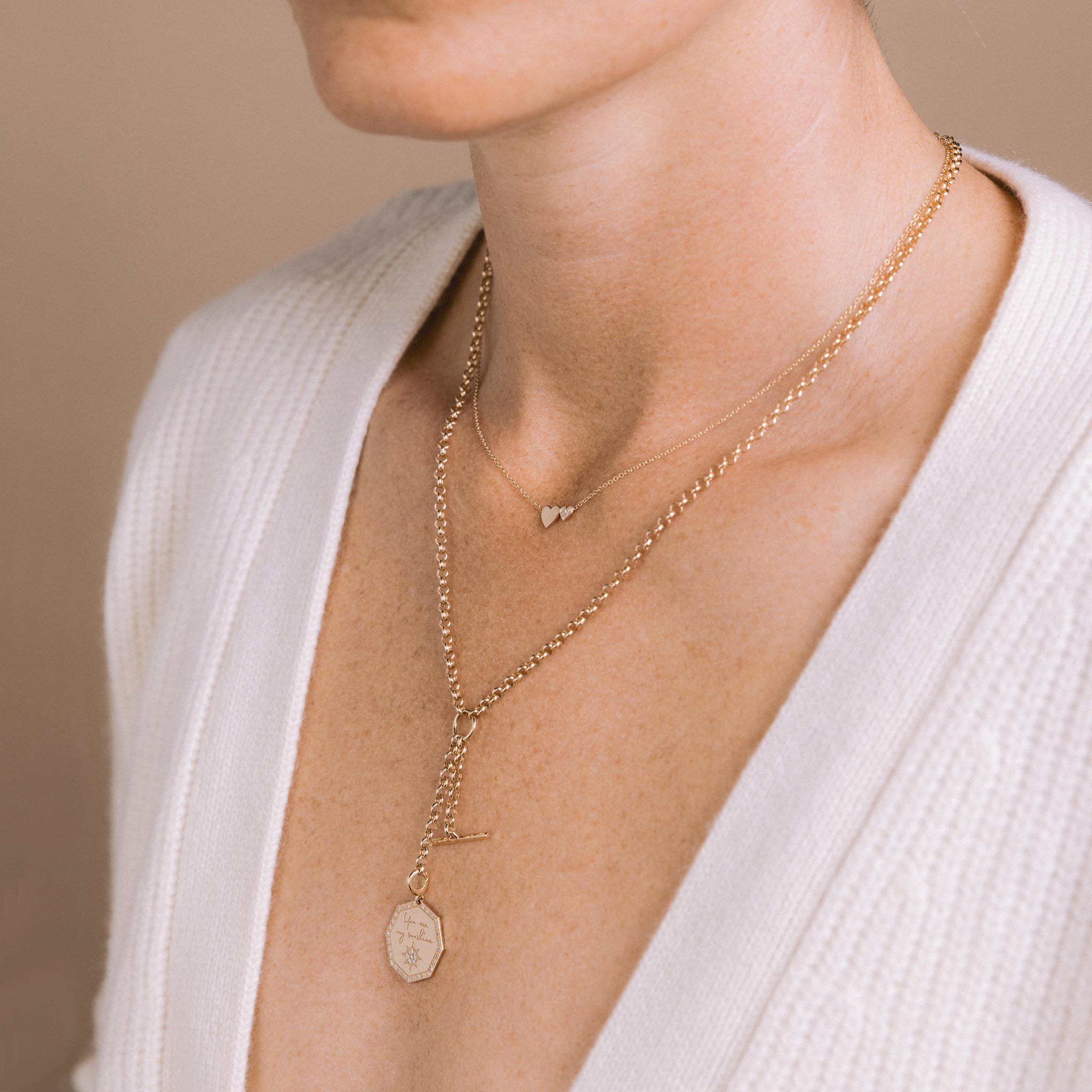 woman in a white sweater wearing a Zoë Chicco 14k Gold  Medium "You are my sunshine" Diamond Octagon Mantra & Toggle Rolo Chain Lariat Necklace layered with a 14k Mixed Midi & Itty Bitty Pavé Diamond Heart Necklace