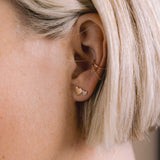 close up of a blonde woman's ear wearing a Zoë Chicco 14k Gold Draped Chain Ear Cuff and a 14k Mixed Midi & Itty Bitty Pavé Diamond Heart Stud Earring layered together