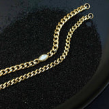 On a black background of sand lies two curb chain bracelets: One of a Kind Marquise diamond bracelet centered on a large curb chain and a medium curb chain with alternating pave diamond links.  