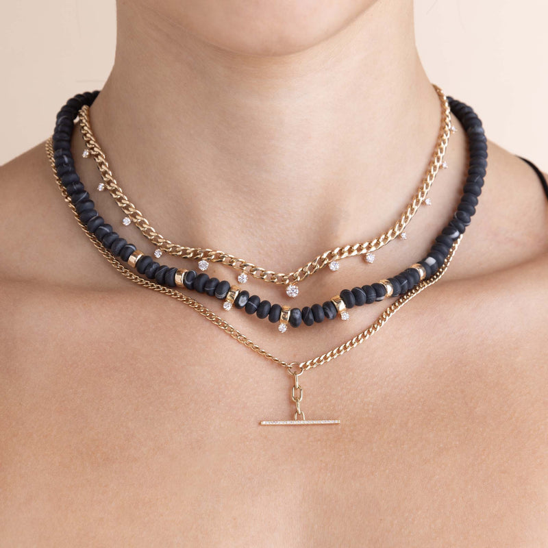 woman wearing a Zoë Chicco 14k Gold & Matte Black Agate Rondelle Bead Necklace with 3 Prong Diamonds layered with a 14k Graduated Prong Diamonds Medium Curb Chain Necklace, and a 14k Mixed Small Curb & Medium Square Oval Chain Pavé Diamond Toggle Lariat Necklace