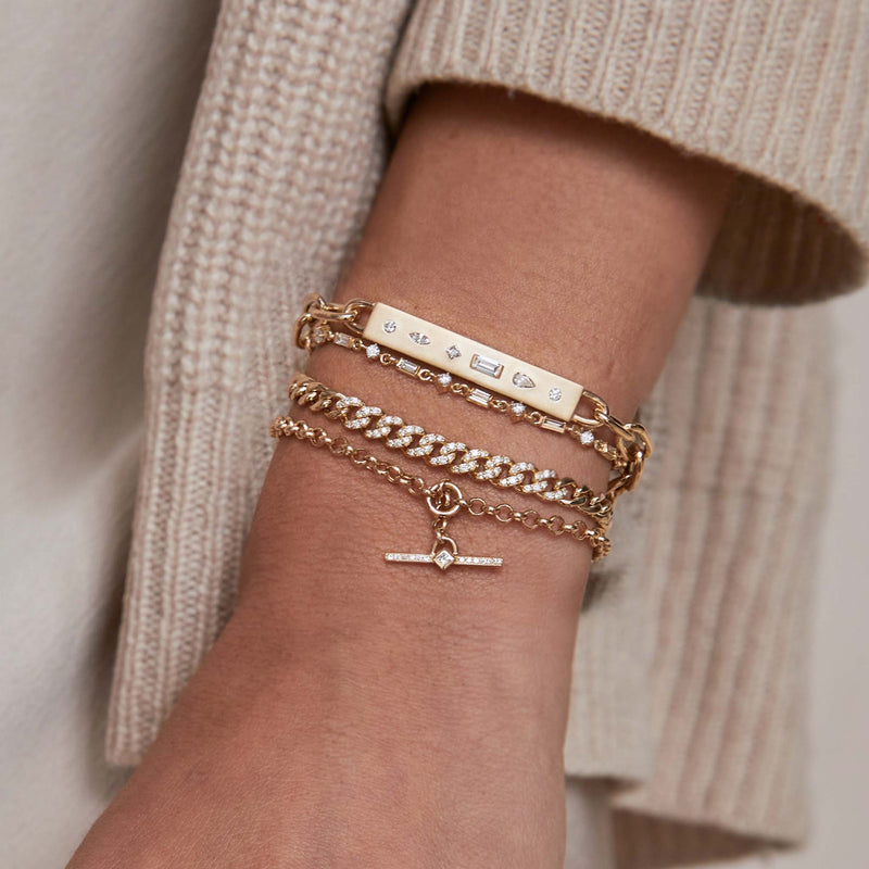 a close up of a woman's wrist wearing a Zoë Chicco 14k Gold Princess Diamond & Diamond Bar Toggle Rolo Bracelet layered with three other bracelets