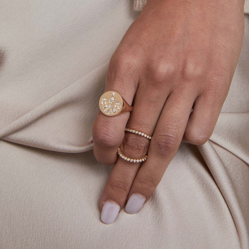 woman's hand against a beige satin background wearing a Zoë Chicco 14k Gold Diamond Mosaic Brushed Gold Round Signet Ring on her index finger