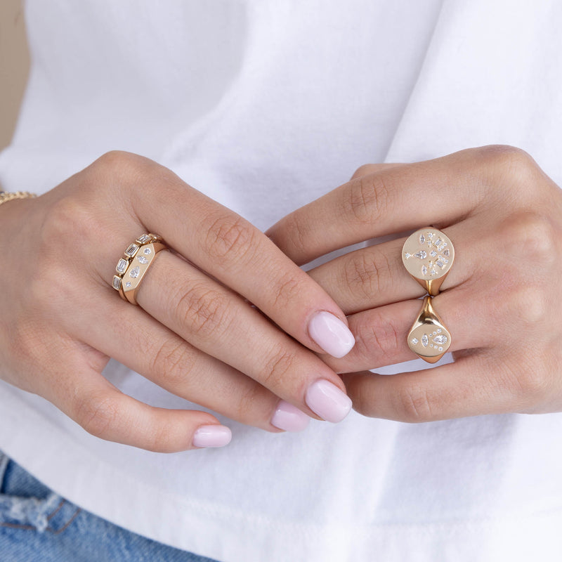 woman in a white shirt with her hands touching wearing a Zoë Chicco 14k Gold 5 Emerald Cut Diamond Bezel Ring stacked with a 14k Diamond Mosaic Brushed Gold Elongated Hexagon Signet Ring on her middle finger of her right hand and two Diamond Mosaic Brushed Gold Signet Rings on her left hand