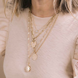 woman in a pink sweater wearing a Zoë Chicco 14k Gold Medium Paperclip Rolo Chain Necklace with Fob Clasp Drop with a Family Locket attached layered with a 14k Gold Large Paperclip Chain Round Enhancer Necklace with a  7 Prong Diamond Pavé Diamond Initials Heart Charm attached and a 14k Medium Mantra with Diamond Border Small Curb Chain Necklace engraved with "Work hard, stay humble, be kind"