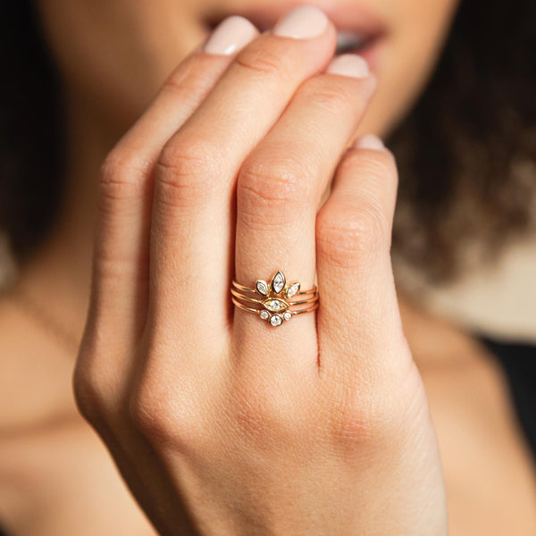 A woman is wearing a Zoe Chicco stack of 3 rings: Marquise Diamond fan ring, an eye ring with diamond, and a graduated bezel diamond arc ring.
