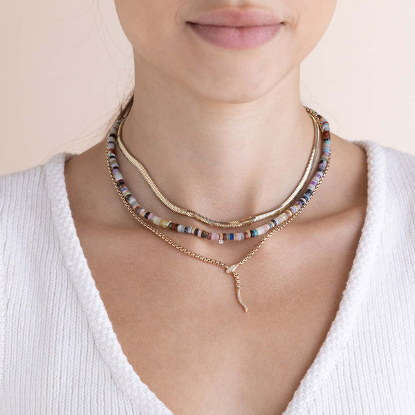 woman in a white sweater wearing a Zoë Chicco 14k Gold & Mixed Gemstone Heishi Bead Necklace with Prong Diamond layered with a Medium Snake Chain Necklace and a Pavé Diamond Serpent Lariat Necklace