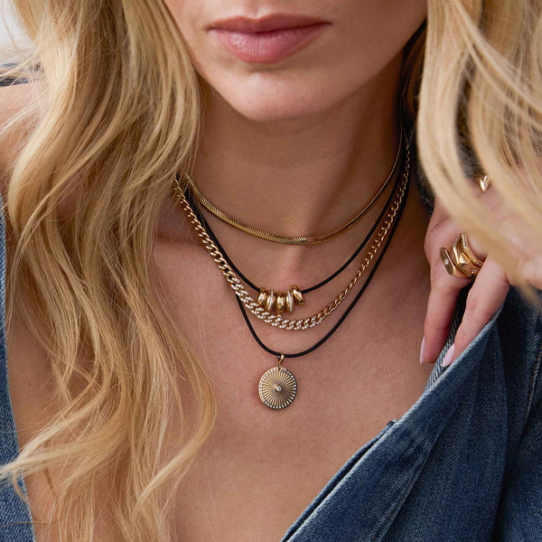 woman in a denim shirt wearing a Zoë Chicco 14k Gold Pavé Diamond Segment Medium Curb Chain Necklace layered with two leather cord charm necklaces and a Medium Snake Chain Necklace