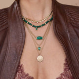 Close-up of layered necklaces 14k Diamond Malachite Barrel Bead Medium Box Chain Necklace, emerald and malachite necklaces, and gold pendants on a person wearing a brown leather 