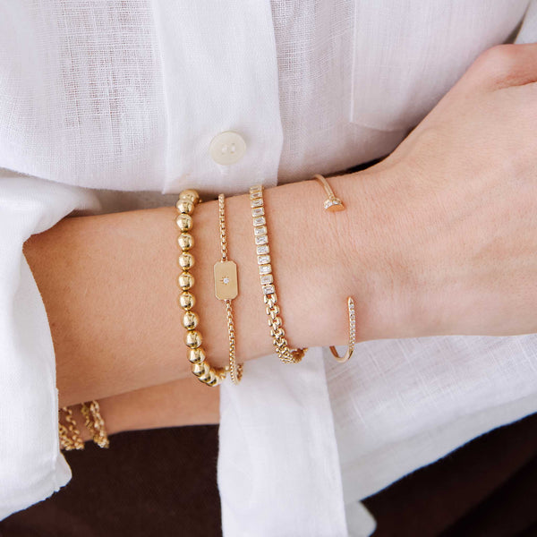 woman in a white shirt wearing a Zoë Chicco 14k Gold Pavé Diamond Nail Cuff Bracelet stacked with a 14k Horizontal Star Set Diamond Square Edge Dog Tag Bracelet and a 14k Gold Ball Bead Bracelet