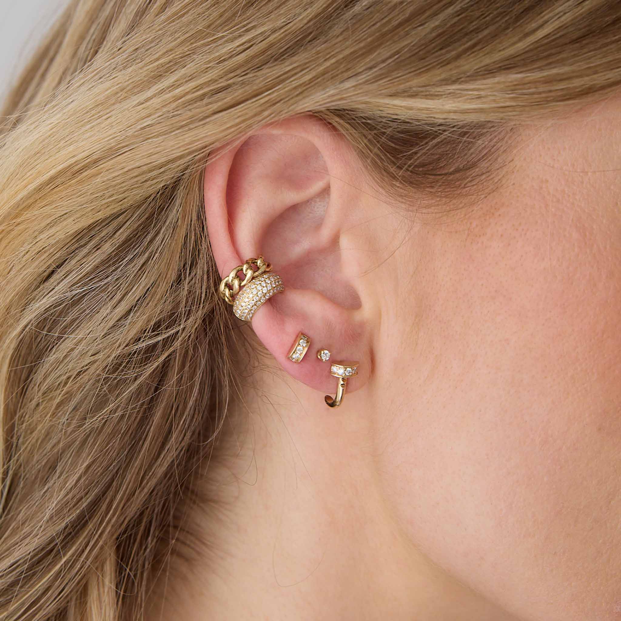 woman's ear wearing a Zoë Chicco 14k Gold Pavé Diamond Nail Half Hoop Earring layered with a diamond stud, 14k Medium Curb Chain Ear Cuff, and a 14k Pavé Diamond Wide Chubby Ear Cuff