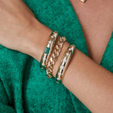 a woman in green holding her wrist up wearing a Zoë Chicco 14k Gold One of a Kind Emerald Cut Emerald & Graduating Diamond Aura Cuff Bracelet layered with two other bracelets