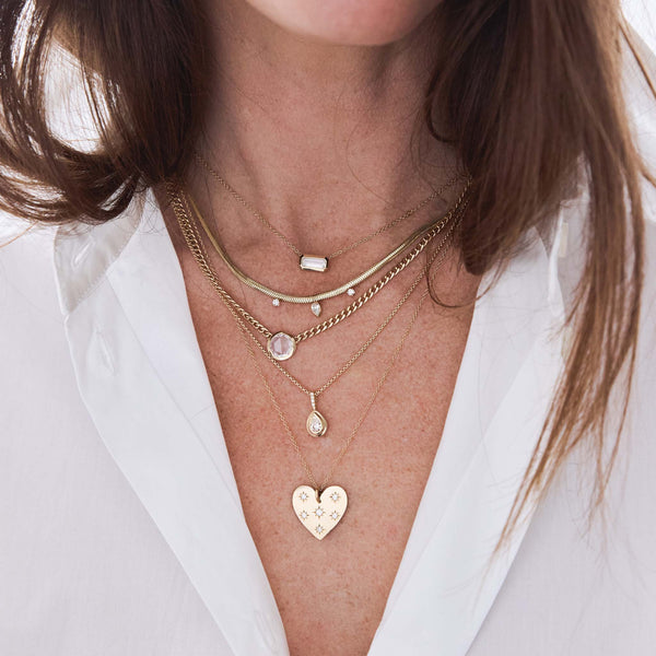 woman in a white shirt wearing a Zoë Chicco 14k Gold Pear & Prong Diamond Snake Chain Necklace layered with a 14k Scattered Star Set Diamonds Aura Heart Necklace and a .49 ctw Horizontal Baguette Diamond Bezel Necklace and a .84 ctw Rose Cut Round Diamond on Small Curb Chain Necklace