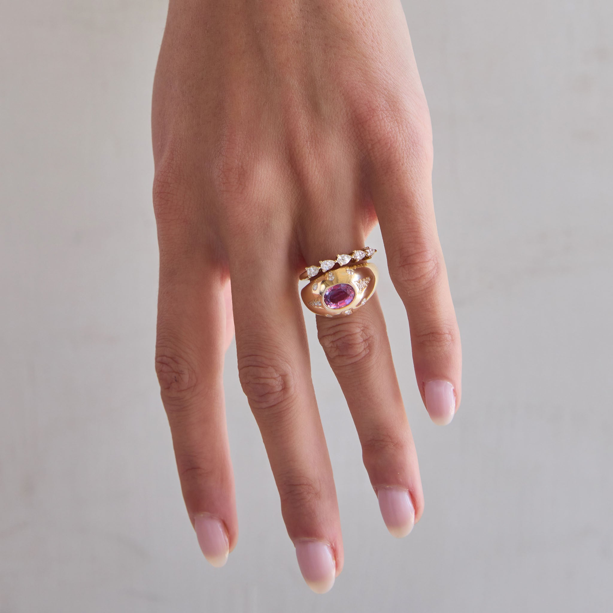 A woman's hand is showcasing the One of a Kind Pink Sapphire Ring and the 5-pear diamond ring.