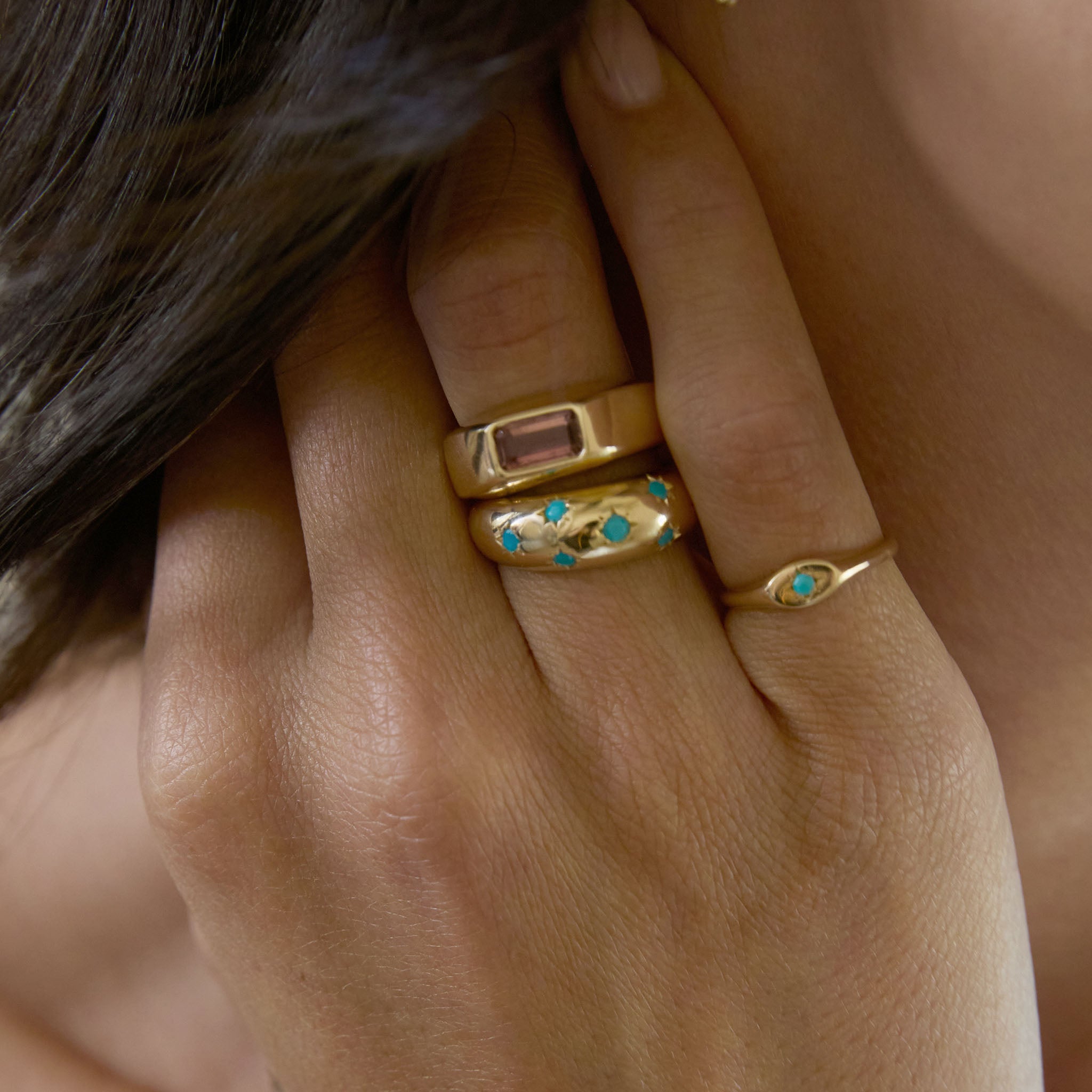 Close-up of a hand wearing Zoe Chicco 14k gold rings with turquoise gemstones and a one of a kind pink sapphire