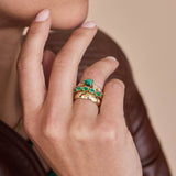 Close up of a hand wearing Zoe Chicco 14k gold rings with diamonds and pear-shaped green emeralds on a neutral background