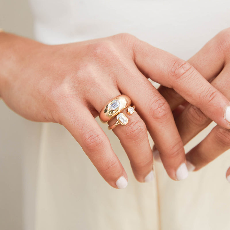 close up of a woman's hand wearing a Zoë Chicco 14k Yellow Gold Pear & Emerald Cut Diamond Bezel Open Ring stacked with a 14k Emerald Cut Diamond Medium Aura Ring on her ring finger