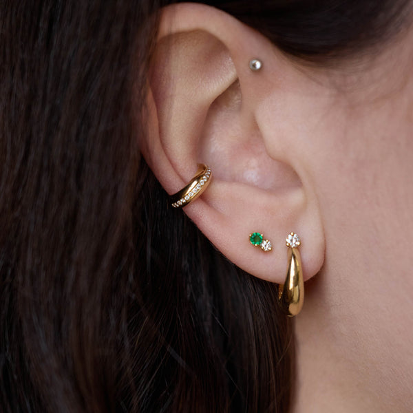 Zoe Chicco 14K Gold Close-up of an ear with gold hoop earrings and a small green gemstone earring.