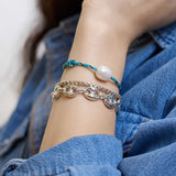Woman in a denim shirt wearing a Zoë Chicco Sterling Silver Large Puffed Mariner Chain Bracelet stacked with a Sterling Silver Large Box Chain Bracelet and a Medium Baroque Pearl Paracord Bracelet