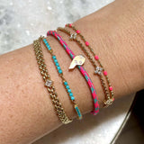 Zoë Chicco 14k Gold Midi Bitty Best Friends Split Left Side Heart Paracord Bracelet in Pink Blue stacked with four other gold colorful bracelets