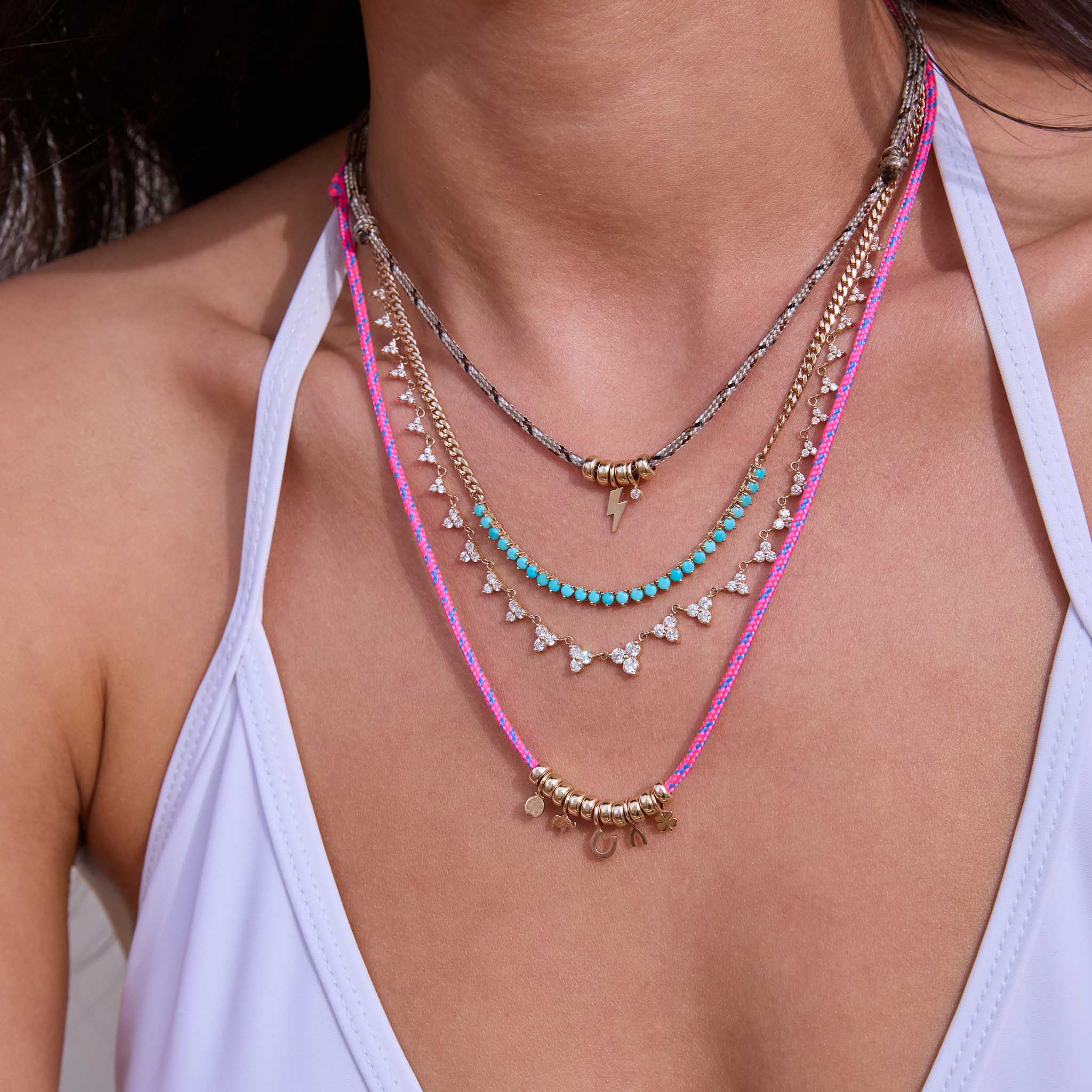 Close up of woman's neck wearing multiple Zoe Chicco 14k gold diamond and turquoise tennis necklaces and pink paracord necklaces