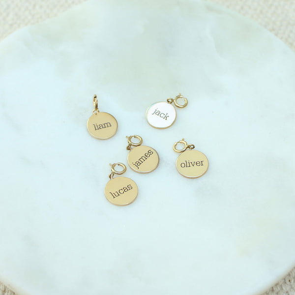 a marble tray with five Zoë Chicco 14k Gold Small Personalized Disc Charm Pendants engraved with different names