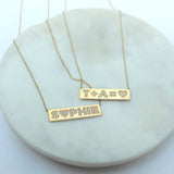 a Zoë Chicco 14k Gold Pavé Diamond Name ID Bar Necklace with Sophie spelled out laid out with another diamond equation ID necklace on a marble tray