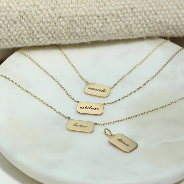 three Zoë Chicco 14k Gold Personalized Rounded Rectangle Nameplate Necklaces engraved with sarah aiden and love laying flat on a marble tray