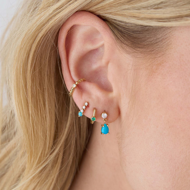 woman's ear wearing a Zoë Chicco 14k Gold Pear Turquoise & Prong Diamond Drop Earring with a 14k Single Emerald Bezel Small Hinge Huggie Hoop in her second piercing, a 14k Prong Turquoise & Short Diamond Tennis Drop Earrings in her third, and a Diamond Bezel Beaded Eternity Ear Cuff