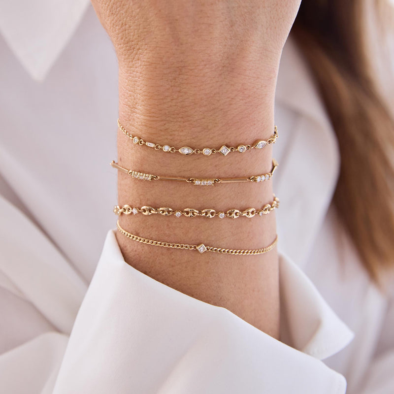 close up of a woman in a white shirt wearing a Zoë Chicco 14k Gold Princess Diamond XS Curb Chain Bracelet layered with a 14k 5 Prong Diamond Small Puffed Mariner Chain Bracelet, 14k Mixed Gold & Diamond Bar Bracelet, and a 14k Linked Mixed Cut Diamond Bolo Bracelet