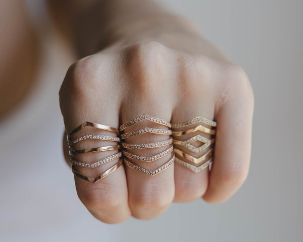 Close-up of a hand wearing multiple Zoe Chicco 14k gold rings with geometric designs on a neutral background