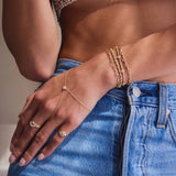 A woman resting her hand on her hip wearing a Zoë Chicco 14k Gold 5 Prong Diamond Quad Station Box Chain Bracelet stacked with three other bracelets