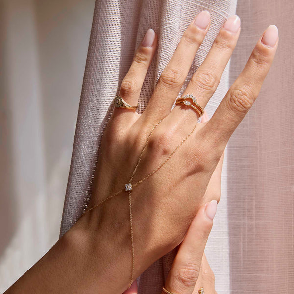 a woman's hand against a light pink curtain wearing a Zoë Chicco 14k Gold Graduated Prong Diamond & Pavé Diamond Double Arch Ring stacked on top of a Prong Marquise Band Ring and wearing a Prong Diamond Quad Hand Chain