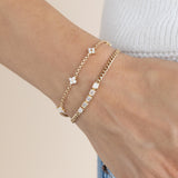 a close up of a woman's wrist resting on her hip wearing a Zoë Chicco 14k Gold 5 Emerald Cut Diamond Segment Curb Chain Bracelet stacked with a 14 Prong Diamond Quad Station Bracelet