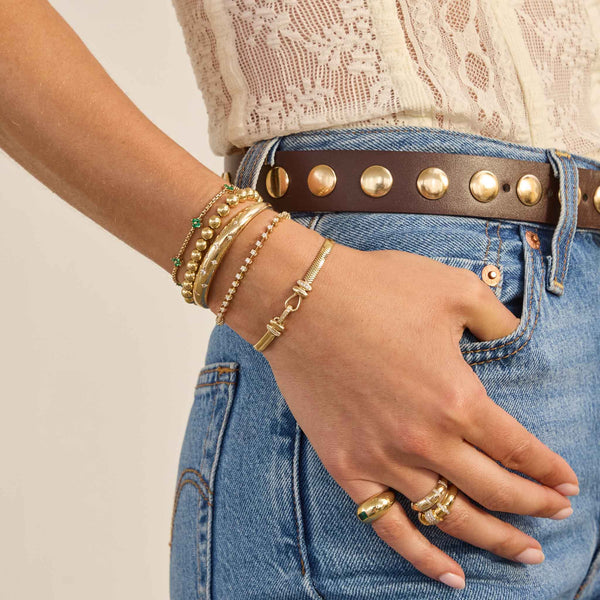 Close-up of a person wearing multiple Zoe Chicco 14kv gold bracelets and rings on a neutral background