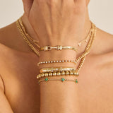 Zoe Chicco 14k gold jewelry including bracelets and necklaces on a person's arm against a neutral background