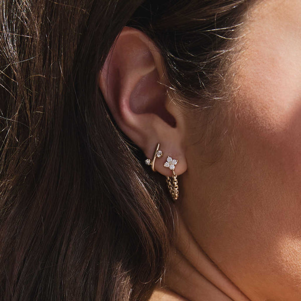 close up of a woman's ear wearing a Zoë Chicco 14k Gold Mixed Prong Diamond J Hook Hoop Earring in her second piercing layered with a 14k Prong Diamond Quad Box Chain Huggie Earring in her first piercing