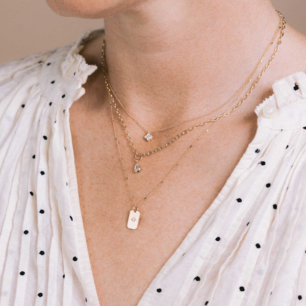 woman in a polka dot shirt wearing a Zoë Chicco 14k Gold Star Set Diamond Small Square Edge Dog Tag Necklace on a Bar and Cable Chain layered with a Prong Diamond Quad necklace and a 14k Pear Diamond Pendant Small Square Oval Chain Necklace
