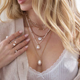 woman in a white pointelle top and sweater wearing a Zoë Chicco 14k Gold Reversible Black & White Diamond Pearl Disc Tan Leather Cord Necklace layered with a 14k 5 Prong Diamond Quad Station Box Chain Necklace, 14k Gold Linked Bar & Graduated Diamond Necklace, and Baroque Pearl Box Chain Necklace