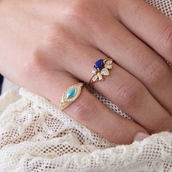 Close up of a hand wearing three Zoe Chicco 14k gold rings with blue gemstones and diamonds against a white lace background
