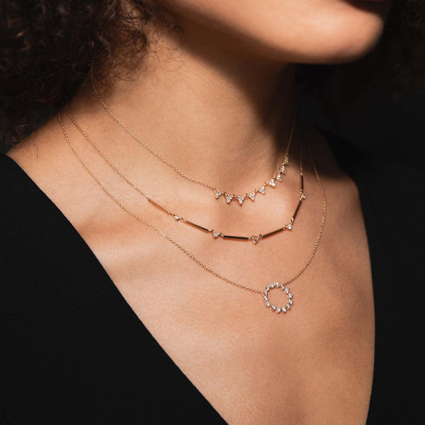A woman in a black shirt is wearing 3 layered diamond necklaces including a linked Prong Diamond Trio Necklace,  Bar with Prong Diamond necklace and a Prong Diamond Circle Necklace.