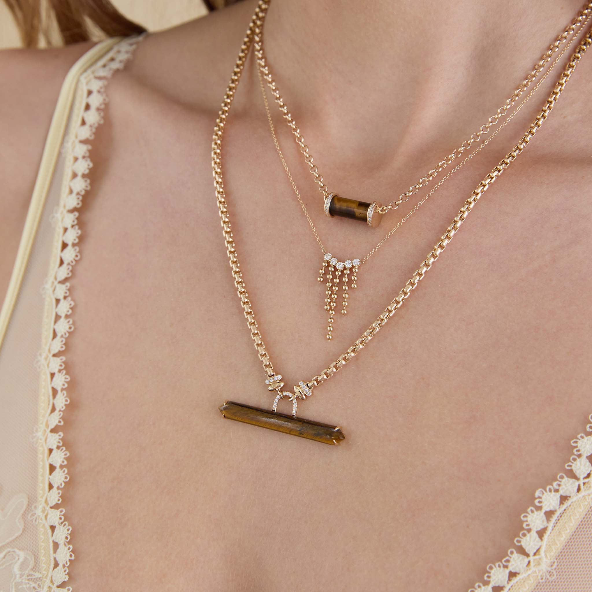 Close-up of a person wearing gold necklaces with gemstones on a neutral background featuring 14k Tiger Eye Bar with Diamonds Large Box Chain Necklace