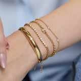 Zoe Chicco 14k gold chain bracelets with small diamonds on a persons wrist with a blurry light blue background