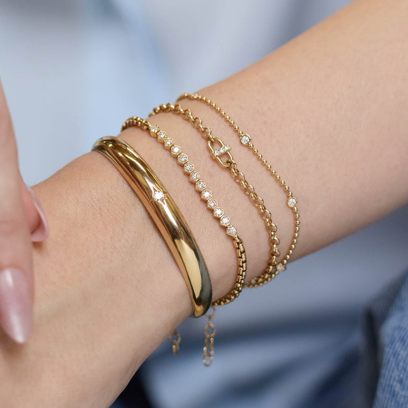 Zoe Chicco 14k gold chain bracelets with small diamonds on a persons wrist with a blurry light blue background