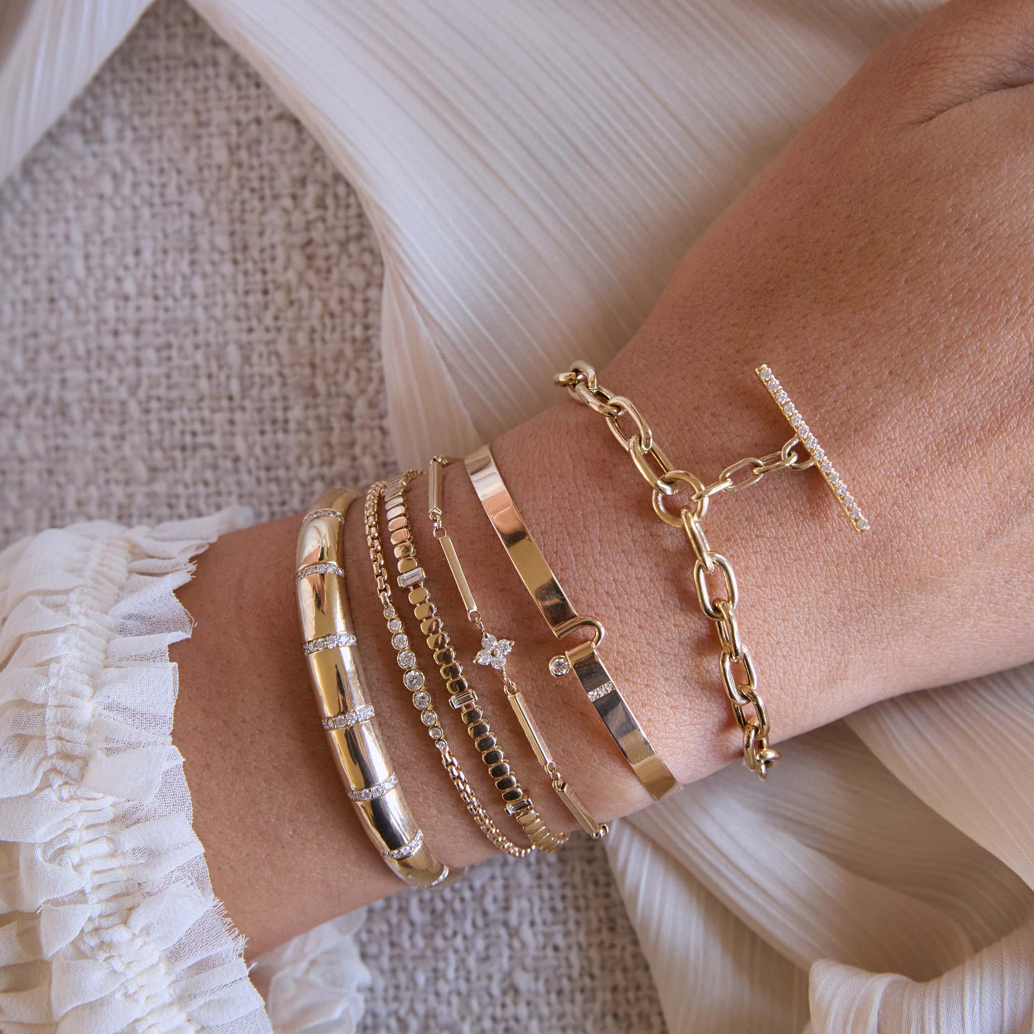 Close-up of a chain bracelet and cuff stack from Zoe Chicco with 14k gold and diamonds against a white textured background