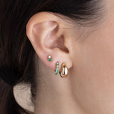 brunette woman wearing a Zoë Chicco 14k Gold Prong Set Emerald Small Hinge Huggie Hoop Earring in her second piercing layered with a Small Aura Huggie Hoop and a 14k Mixed Prong Emerald & Diamond Stud Earring in her third piercing