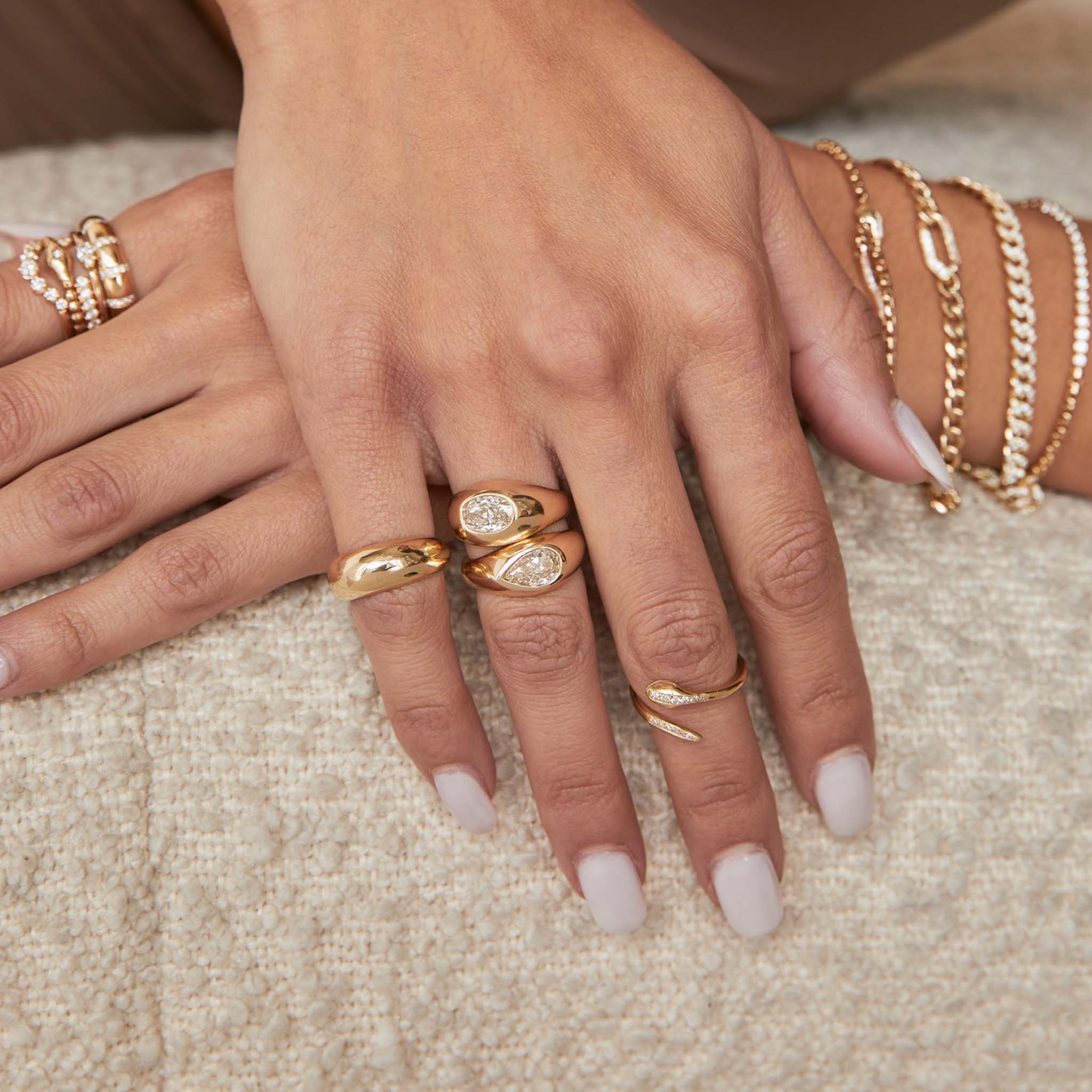 woman resting her hand on a sofa wearing a Zoë Chicco 14k Gold One of a Kind Champagne Pear Diamond Signet Ring layered with another one of a kind diamond ring on her ring finger