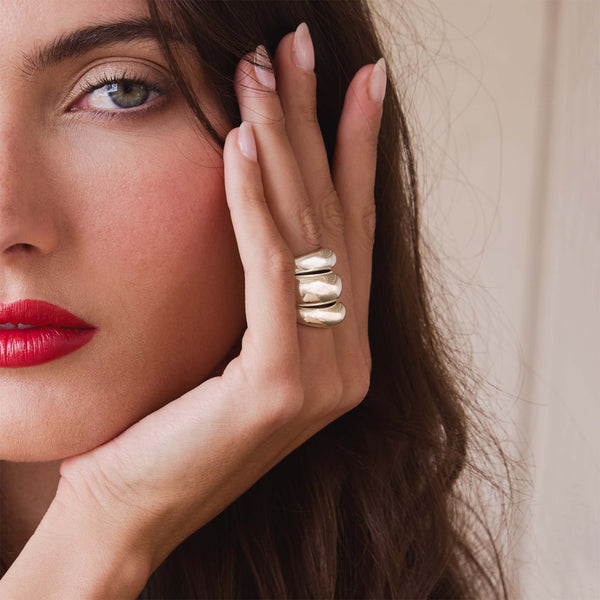 brunette woman resting her hand against her face wearing two Zoë Chicco Sterling Silver Small Aura Rings with a Sterling Silver Medium Aura Ring in the middle stacked together on her ring finger