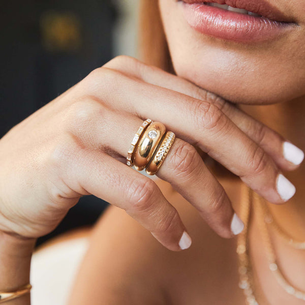 Woman's hand resting under her chin wearing a Zoë Chicco 14k Gold 10 French Set Diamond Half Round Ring stacked with a Baguette Diamond Eternity Ring and a Round Diamond Small Aura Ring stacked together on her ring finger
