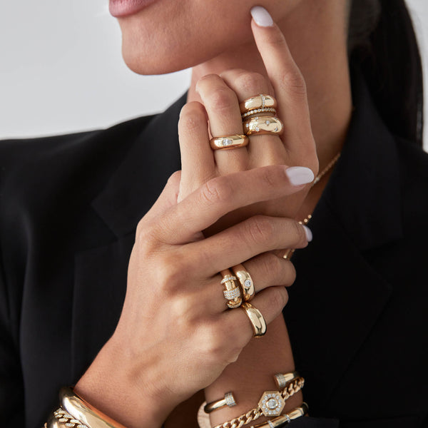 woman in a black blazer with her hands clasped together wearing a Zoë Chicco 14k Gold Pavé Diamond Banded Door Knocker Half Round Ring stacked with an aura ring on her ring finger
