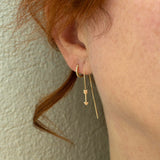 A woman is wearing Zoe Chicco's 14k Gold Arrow Chain Drop Threaders and pave hinged huggies